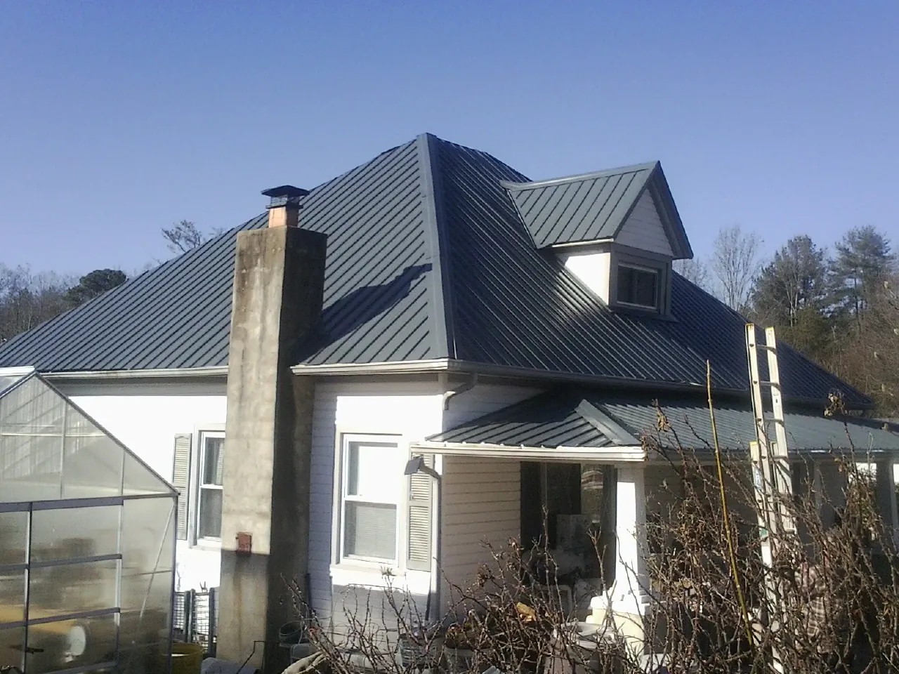 Dark blue standing seam metal roof on a white farmhouse with dormer — Slate & Tile Roof Repair by Roofing Brothers in La Grange