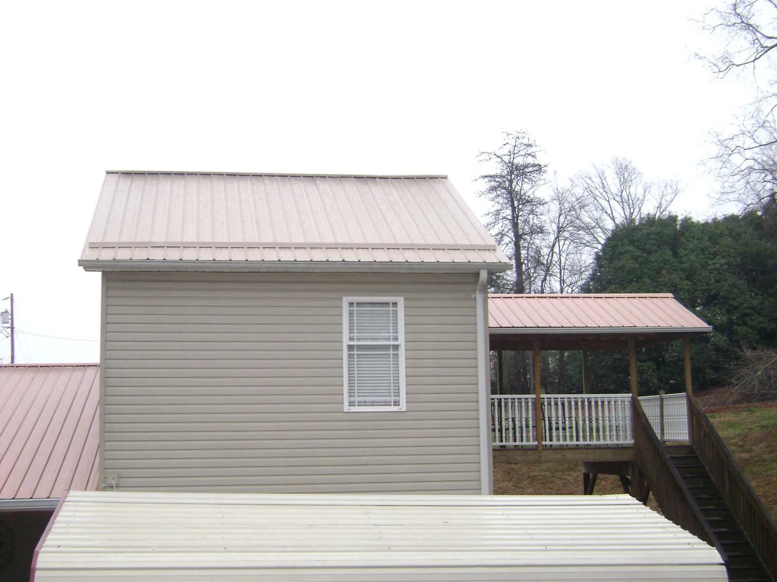 Tan metal roofs on a two story addition and attached porch, from a Roof Replacement job in La Grange